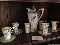 Full view of Prussian tea set with teapot, 6 cups, and 6 saucers on a dark wooden shelf, showing floral and gold decorative elements