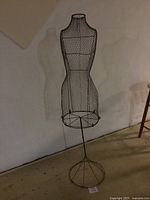 Full body view of the wire framed female seamstress mannequin on circular wire base stand.