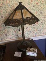 Full view of Tiffany style metal lamp on table with decorative hunting scene box beside it.