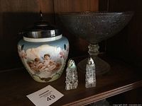 Showing all four items together: vase with cherub painting and lid, decorative glass bowl on stand, and salt and pepper shakers with visible corrosion on salt shaker top.