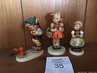 Front view of three Hummel figurines: boy with rabbit, girl with basket, girl with bouquet.