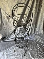 Front view of the entire 3-tier cast iron wire basket stand showing all three circular baskets and decorative scrollwork legs.