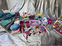 Overview of Barbie beds, chairs, pet accessories, sofa, and various doll accessories arranged together