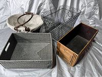 Three baskets shown together on a grey backdrop: grey synthetic woven basket with built-in handles, black wire mesh basket, bamboo basket with black lining.