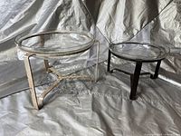 Two round cake stands with glass tops and metal frames, set on a gray fabric background, showing overall shape, size and condition.