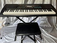 Full view of Casio CT-S200 keyboard placed on X-style metal stand with black padded seat in front on a grey fabric backdrop.