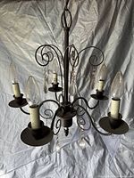 Photo showing the smaller metal chandelier with candle-style bulbs and hanging crystals against a white backdrop.