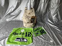 Beige canvas drawstring flag football bag with attached card, two Seattle Seahawks towels laid flat in front, green towel with large logo and text, blue towel with smaller logo and text