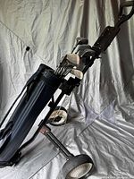 Side angle of navy blue Top Flight golf bag with attached push/pull golf cart showing clubs inside the bag and cart wheels.