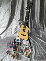 Full lot setup showing acoustic guitar on stand surrounded by strap, picks, tuner, capo, accessory pack, and chord books