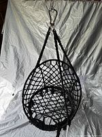Black hanging rope chair with netted seat and backrest suspended from braided ropes, photographed against a gray backdrop.