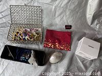 Photo of clear bubble-patterned rectangular storage box, red XOXO pouch, silver oval trinket box, small white Monrio box, and a small dark rectangular container on a silver surface