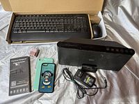 Lot contents showing keyboard in box, Bluetooth speaker with charger, phone cases, screen protector, and charging adapter