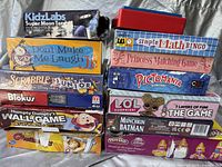 Various new/unopened kids board games stacked including Scrabble Junior Disney Edition, KidzLabs Super Moon Torch, Play-Doh Magical Designer Pack