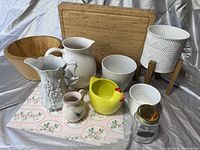Photo showing bamboo cutting board, wooden salad bowl, several ceramic pitchers, pots, and decorative plant pot with wooden stand.