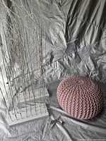 Image of one LED white grass planter with rectangular white base and visible wiring cord, alongside a pink knit pouffe.