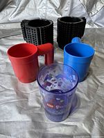 Lot of five LEGO themed cups and mugs including two black brick-style mugs, one red mug, one blue mug, and one translucent purple LEGO Friends cup