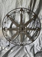 Full front view of the large round metal wall hanging showing circular frame with eight spokes and ornamental scroll and floral details.