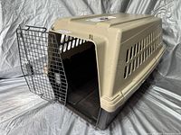 Large pet carrier with beige top and dark brown base, metal wire door open, shown on gray cloth background