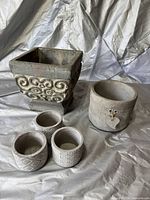 Five decorative planter pots arranged on a fabric backdrop showing different sizes and carved textures.
