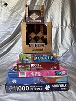 Photo showing a stack of puzzles including Ravensburger and Pure Genius wooden brain teaser puzzle.