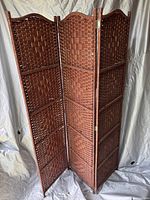 Full view of the 3-panel woven room divider in reddish-brown with curved tops, standing upright.