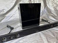 Samsung soundbar and subwoofer set shown on white fabric background with power cords visible.