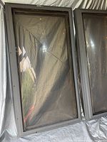 Two rectangular skylights with dark gray metal frames, placed side by side on a gray tarp, seen from above.