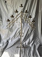 Full view of the tall metal candelabra showing seven arms for candles and its tripod base against a white backdrop.