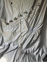 Full view of the tall metal candelabra with multiple flower-shaped candle holders and scroll design, showing off-white aged paint.