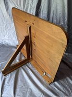 Angle view of wooden table showing folding support leg and wall-mounting brackets.