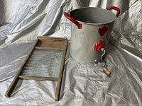 Wooden washboard with a metal scrubbing surface and a metal butter churn with red handles and spout.