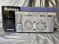 Front view of boxed Holmes electrically reversible window fan showing product image and branding.
