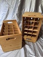 Two wooden crates side by side on a neutral fabric background. Both crates have multiple compartments for holding bottles.