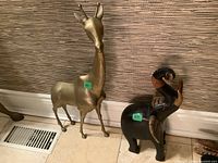 Metal giraffe and wooden elephant sculptures side by side on tiled floor against wall.