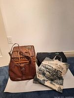 Full view of brown leather handbag, wicker picnic basket, and Edinburgh tote bag placed on a floor.