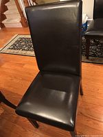 Front view of single black upholstered wooden dining chair showing seat and backrest