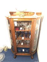 Front view of oak china cabinet showing curved glass sides, brass knob, and three interior shelves.