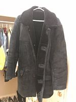 Black shearling-lined suede leather jacket hanging in closet