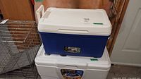 Two coolers stacked: blue and white Igloo cooler on top, white Coleman cooler below.