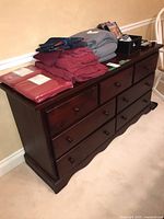 Full view of dark stained wood dresser with nine drawers and several folded clothing items on top.