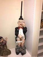 Full front view of resin man holding toilet paper roll, plunger handle extends from head