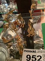 Seven artisan figurines made of metal and crystal including flying horse, seahorse, rooster, and bird shapes on glass shelf.