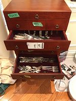 Wooden flatware chest open showing silver plated flatware inside drawers, organized by type.