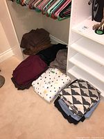 View of various folded linens stacked on floor including brown, gold, black, maroon, gray, star-themed white sheet, and a geometric black and white sheet.