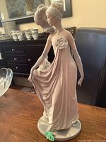 Front view of the Lladro bisque finish 1920s style flapper figurine on wood surface, showing dress and flower detail.