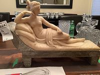 Full side view of the pink-hued marble figure on the settee base among glassware