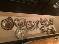 Overview photo showing all metal serving pieces arranged in a drawer, including shell dishes, dolphin bottle opener, apple salt and pepper shakers, and small accessories.