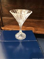 Single martini glass in fluted crystal design resting on navy Mikasa box, wood backdrop.
