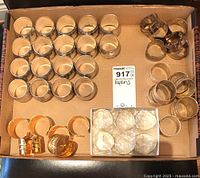 Various napkin holders arranged in cardboard box showing silver, gold and clear glass/acrylic styles